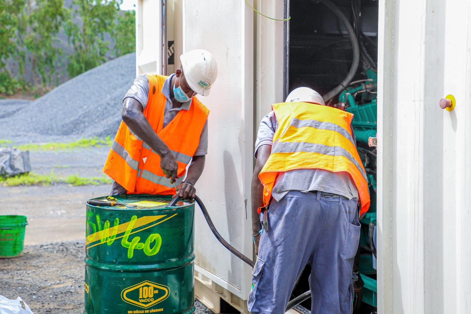 Deux techniciens SEEE font la vidange d'un groupe électrogène en conteneur